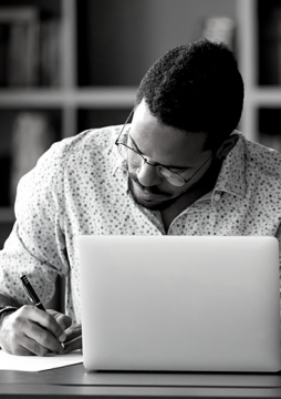 Person writing at a desk with an open laptop