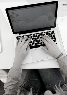 Person typing on a laptop at a desk with papers and a notebook nearby.