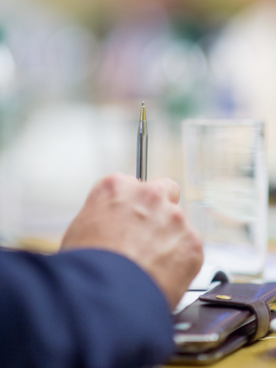 Close-up of a hand holding a pen near a glass of water and documents
