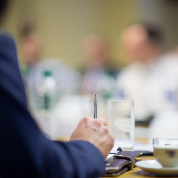 Close-up of a hand holding a pen at a table with water bottles and glasses