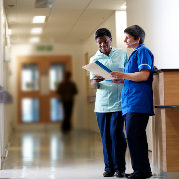 Two healthcare professionals discussing documents in a well-lit hallway