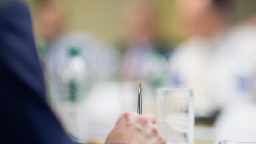 Close-up of a hand holding a pen near a glass of water and documents
