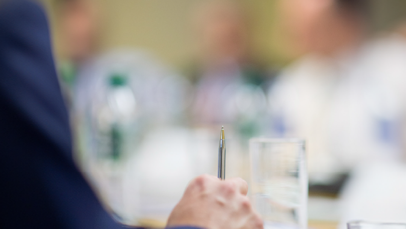 Close-up of a hand holding a pen at a table with water bottles and glasses