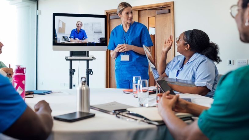 Healthcare professionals in a meeting with one person speaking and another joining via video call.