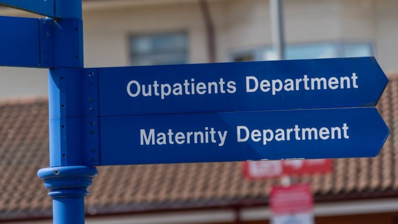 signpost with two directional signs: the top sign points to the 'Outpatients Department' and the bottom sign points to the 'Maternity Department'.